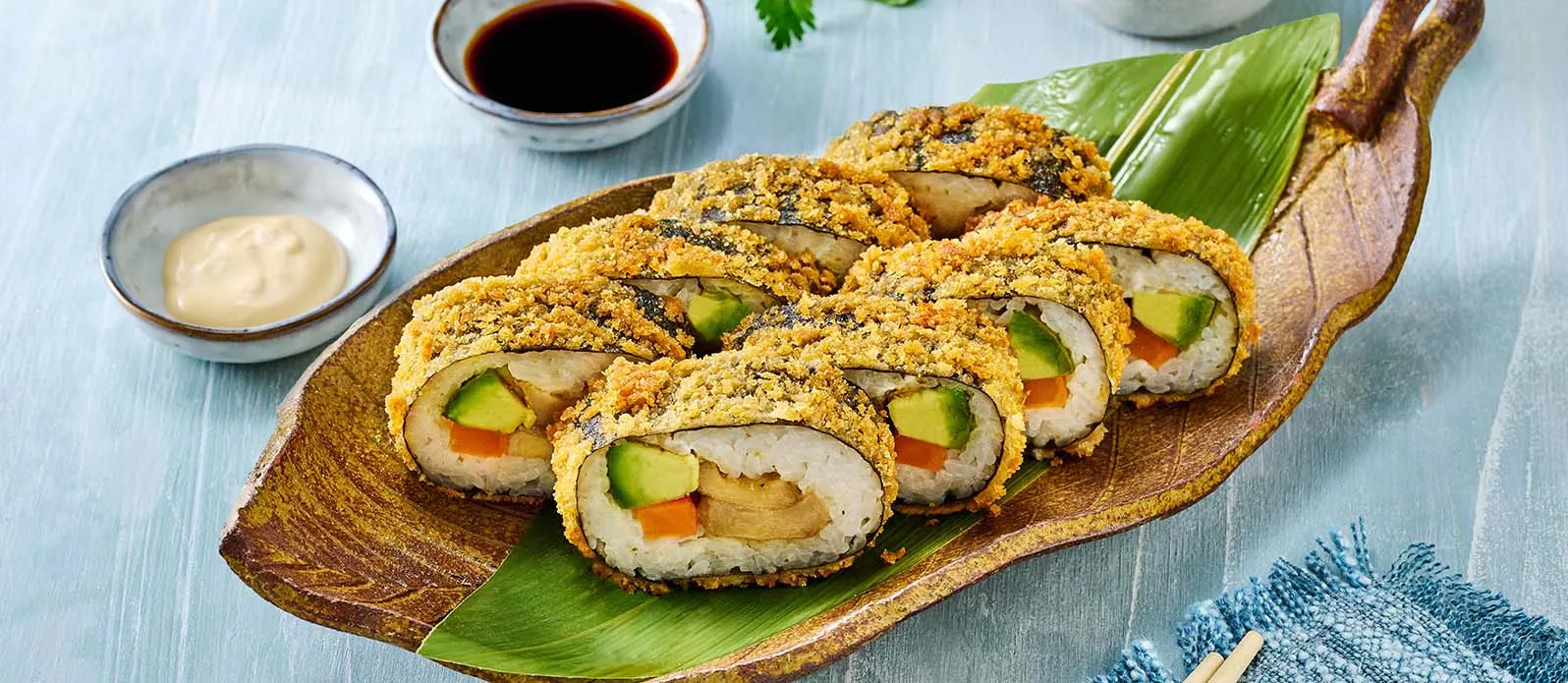 Vegane Sushi-Rollen mit Tempura auf einem Bananenblatt angerichtet.