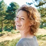 Lächelnde Frau im natürlichen Outdoor-Portrait vor grüner Parklandschaft