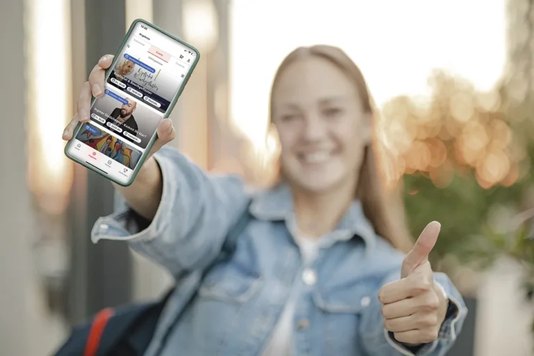Junge Frau zeigt lächelnd ein Smartphone und den Daumen nach oben.