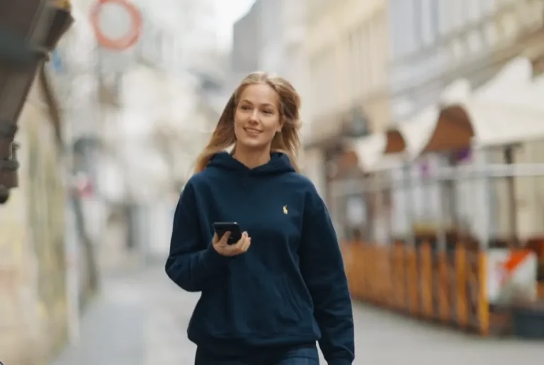 Junge Frau mit Smartphone geht durch eine Einkaufsstraße.
